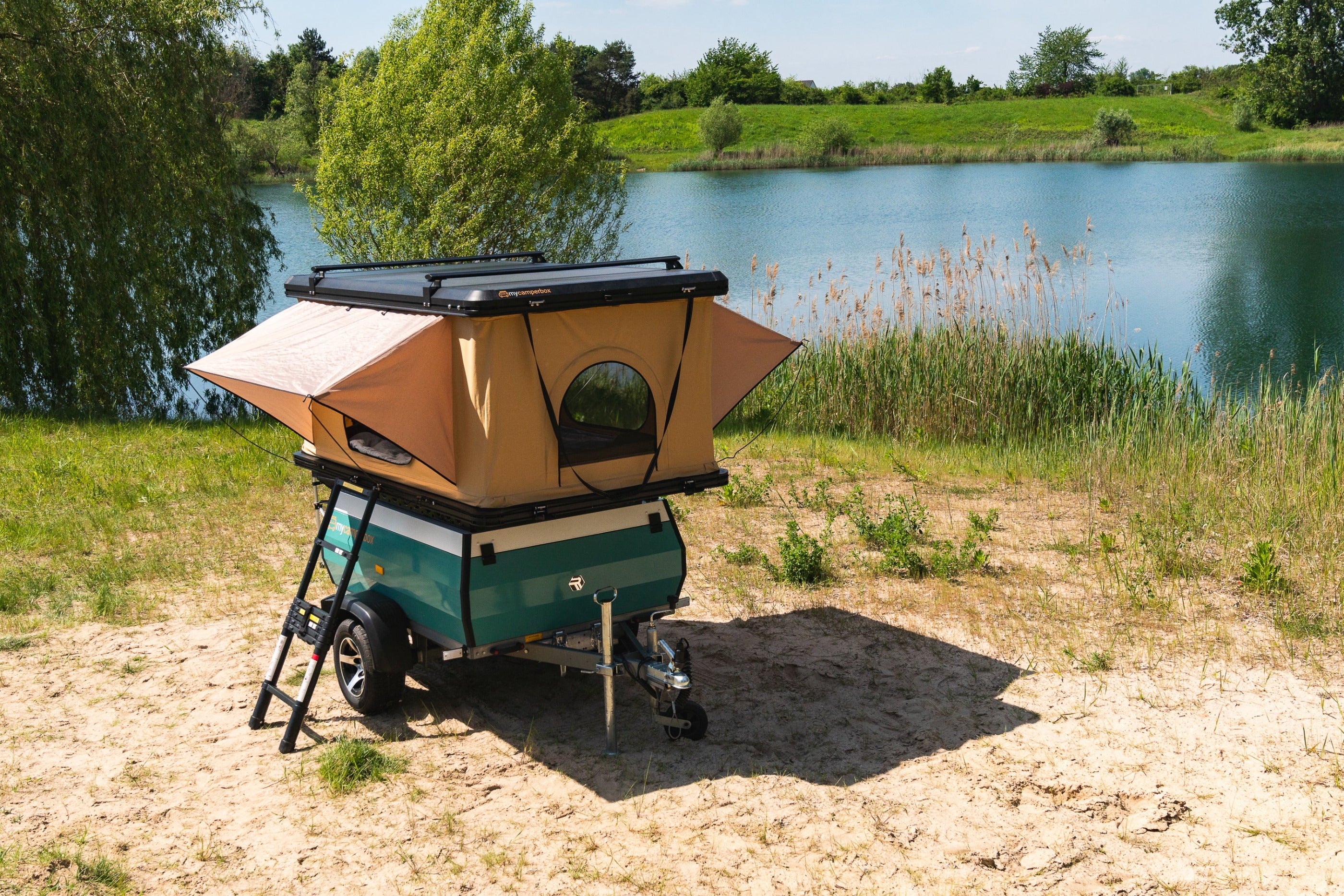 Vario Mini-Wohnwagen in individueller Farbe mit Auto-Dachzelt an einem schönen See zum Camping.