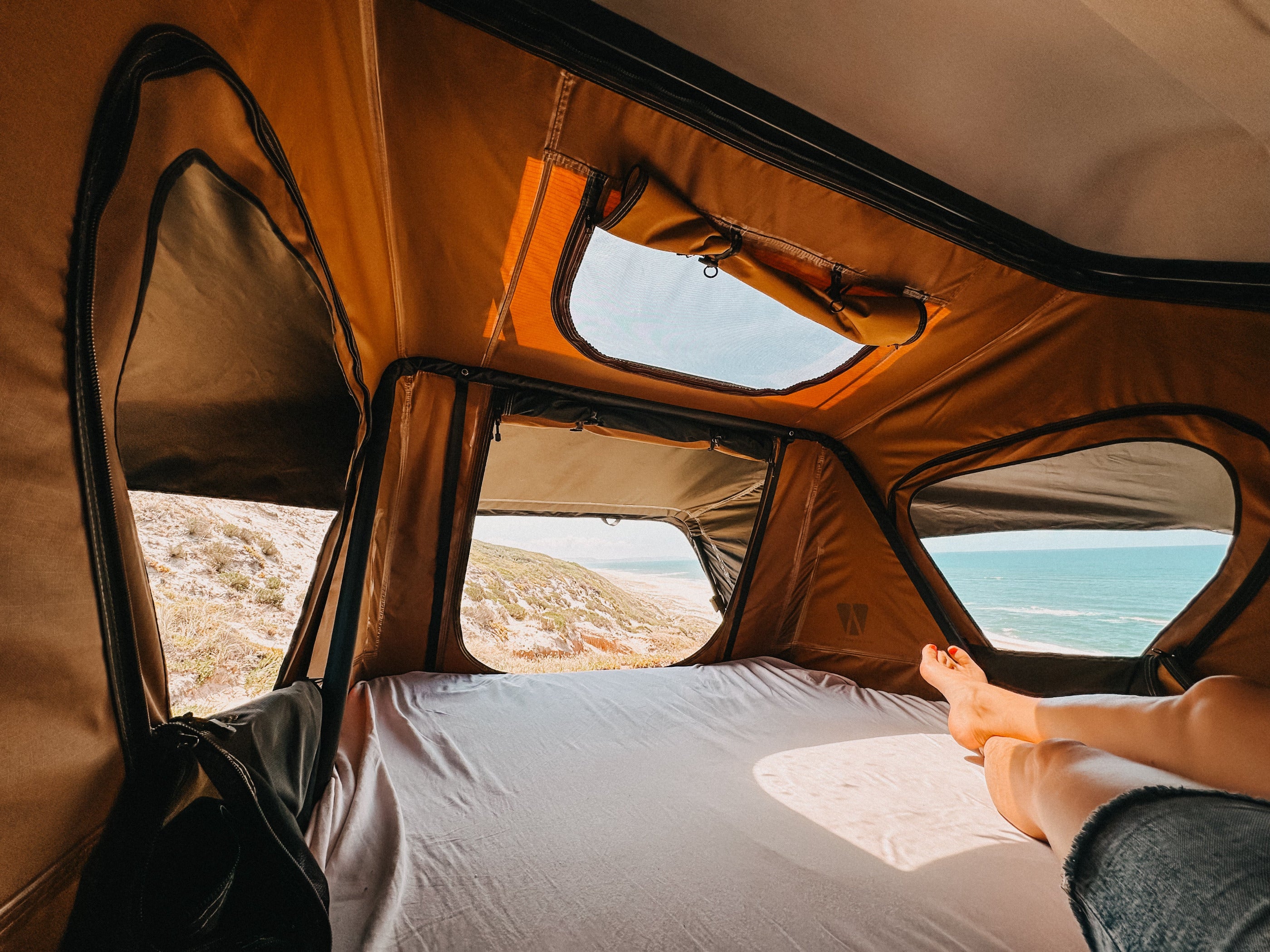 Auto-Dachzelt Innenansicht mit geöffneten Fenstern und Blick auf Meer und Strand
